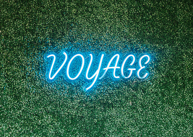 green wall with neon sign that says voyage